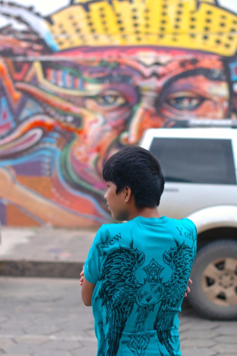 A young Bolivian kid, waiting for a cab in front of some pretty cool graffiti.  
